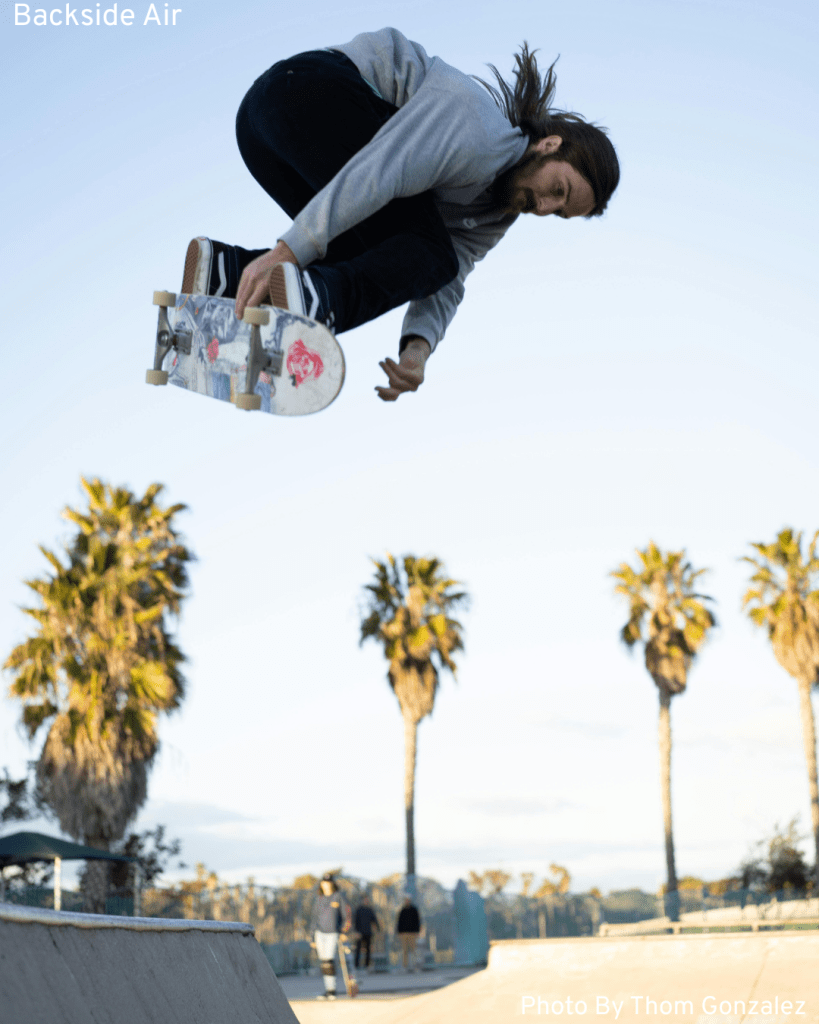 A skilled skateboarder performs a backside air trick, displaying courage and commitment as he soars through the air.