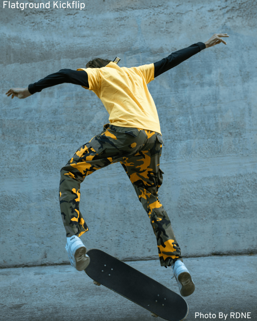 A young Black skater executing a flatground kickflip, captured in action on his skateboard.