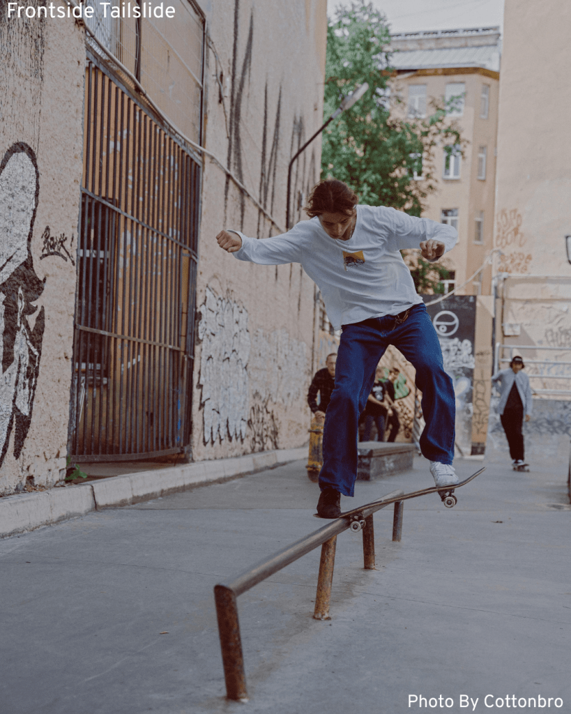 A man skillfully does a frontside tailslide on a rail, surrounded by friends enjoying the street skate scene.