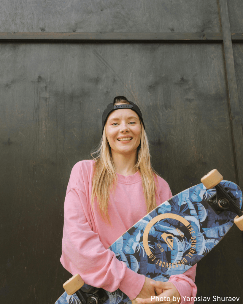 A cool girl in a pink shirt proudly holds her skateboard, showcasing her surfskate style.