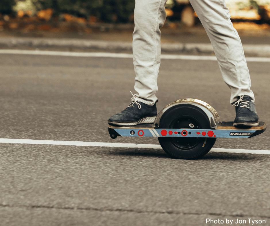 An adult confidently rides a onewheel skateboard along the street, demonstrating his skills and control.